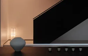 A minimalist living room featuring wooden elements, a lit lamp, and five small white cups arranged on a wooden surface.