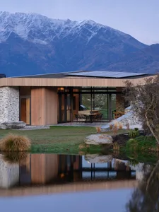 A modern house with wooden siding, concrete patio, and glass windows reflecting the natural surroundings.