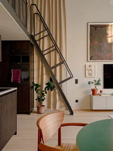 Modern loft interior with a steel ladder leading to a mezzanine level, featuring a kitchenette, wooden floor, and potted plan