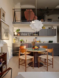 A modern residential kitchen with wooden elements, featuring a dining area with a green table and wooden chairs, and a counte