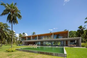 A modern residential pool house with a concrete exterior and a large swimming pool surrounded by a well-manicured lawn and su