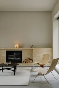 A minimalist living room with a stone fireplace, candles, and chairs.