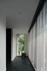 A minimalist bedroom featuring textured curtains and a dark floor, with a decorative skull on a table.