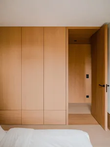 Minimalist, modern bedroom featuring sleek wooden cabinets and a white bed.