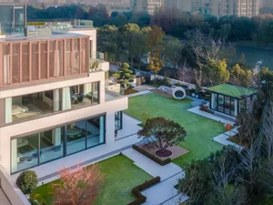 A modern house with a spacious outdoor garden featuring glass walls, concrete patio, and green lawn.