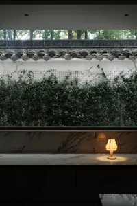 A modern minimalist interior with concrete walls, greenery, and a lit lamp.