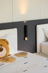 A modern minimalist bedroom featuring a fabric bed with metal headboards and a decorative teddy bear.