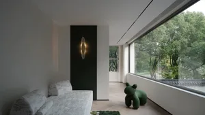 Contemporary minimalist living room featuring a sleek sofa, green animal-shaped ottoman, and a large window overlooking lush 