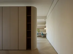 A modern minimalist office space with a wooden floor and sleek, curved white cabinets.