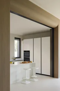 Modern minimalist kitchen with white cabinetry and sleek stainless steel appliances, featuring a central island and stools fo