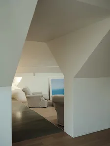 A modern living room featuring wooden flooring and concrete walls, with a comfortable armchair and a framed artwork.