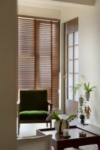 A minimalist living room with wooden blinds, a green accent chair, and a modern coffee table with plants and a vase of tulips