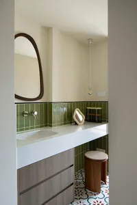 Modern bathroom with green tiles, white countertop, and wooden stool.