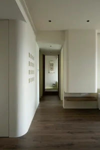 A modern, minimalist corridor with white walls and a wooden floor.