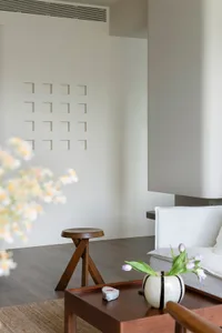 A modern minimalist living room with neutral tones, featuring a white sofa, wooden stool, and decorative vase with tulips.