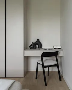 A minimalist office desk area with a black chair, white desk, and decorative black vases.