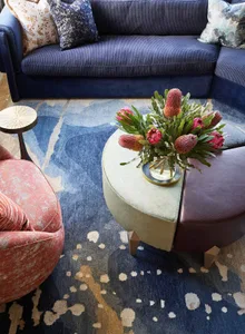 Industrially themed living room featuring a blue couch, floral arrangement, and wooden coffee table on a patterned rug.