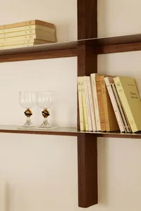 A modern bookshelf made of wood with books and wine glasses.