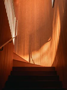 A wooden staircase with light filtering through railings, creating shadow patterns on the wall.