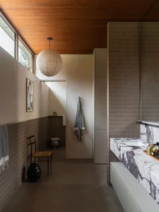 A modern bathroom featuring a marble sink counter and tiled walls with a paper lantern hanging from the ceiling.