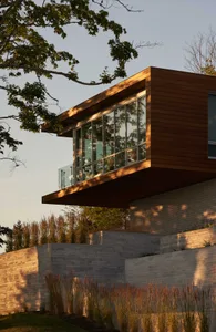 A modern house with a wooden exterior and brick retaining walls, casting shadows on the surrounding landscape.