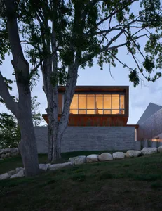 A modern house with large glass windows and a tree in the foreground.