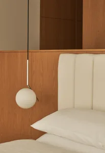 A modern minimalist bedroom featuring a wooden wardrobe and upholstered headboard with plush pillows.
