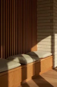 Modern window seat with wooden slatted wall and brick column, featuring cozy cushions.