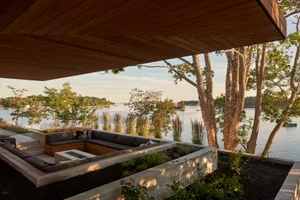 Outdoor lounge area with built-in seating and fire pit overlooking a calm waterfront.