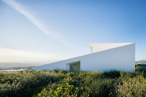 A contemporary white house with large windows set against a clear blue sky.