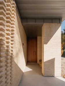 A modern building entrance with a wooden door and a textured brick wall.