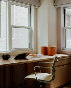 A minimalist industrial home office featuring a wooden desk with a leatherbound notebook, orange containers, and a white chai