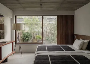 A minimalist bedroom with a large window, natural lighting, and a wooden headboard.