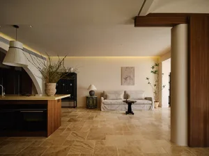 Neutral-toned minimalist living room with a plant on a side table, a beige sofa, and a kitchen island in the foreground.