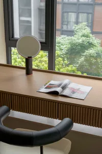 A modern desk scene featuring a wooden desk, a round mirror, an open magazine, and a black and white chair with a white cushi