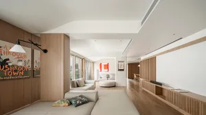 Modern living room interior featuring a beige sofa with cushions, a white ottoman, and a wooden floor with integrated ceiling