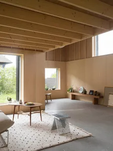 A minimalist living room with natural wood elements, featuring a coffee table, rug, and concrete floor.