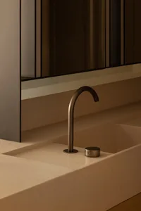 Modern minimalist bathroom featuring a sleek metal faucet mounted on a flat sink surface, set against a warm, neutral-colored