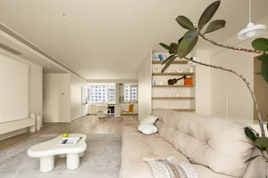 A minimalist living room with a beige couch, white coffee table, and a plant.