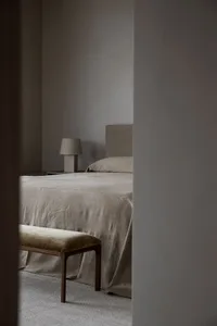 A minimalist bedroom featuring a bed with neutral-colored fabric bedding and a wooden bench.