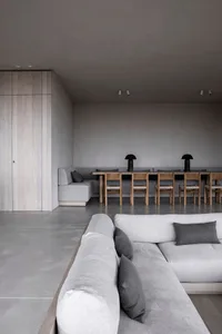 Minimalist living room with concrete floor and furniture, featuring a concrete sectional sofa and a wooden dining table with 