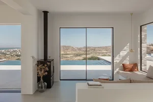 Modern minimalist living room with large windows overlooking the mountains and sea, featuring sleek concrete finishes and sim