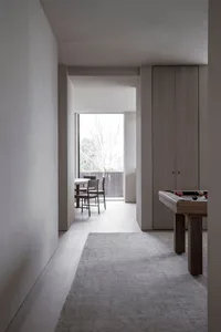 A modern minimalist living room featuring a wooden floor, minimalist furniture, and a large window with a view of trees.