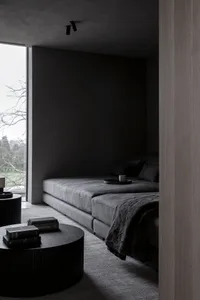 A modern minimalist living room with a large sofa, coffee tables, and a window view of nature.