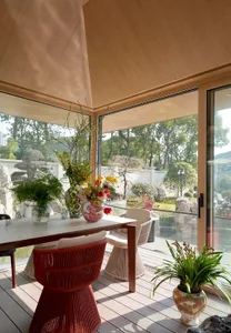 A modern patio with a wooden table, red chair, and flower arrangements in vases.