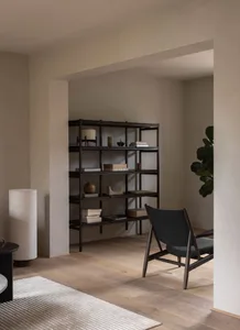 A minimalist living room featuring a wooden shelving unit with books, decorative objects, and a large chair with dark fabric 