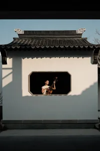 A person playing a traditional Chinese instrument in a window of an ancient building.