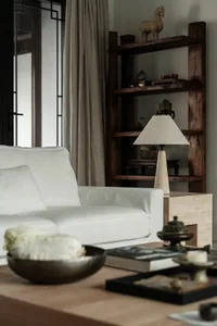 Modern living room featuring white sofa, wooden shelving unit, and concrete side table with books, candles, and decorative it