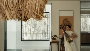 A minimalist interior with a white cloth suspended from the ceiling, a woman playing a guitar, and a framed artwork on the wa