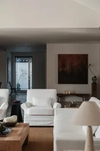 A modern, minimalist living room with white upholstered furniture and warm, neutral-toned decor.